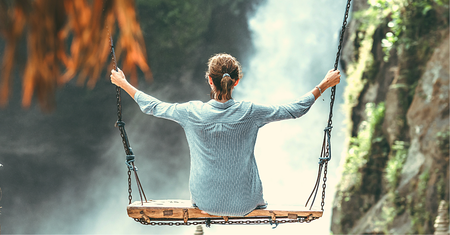 A woman balances on a swing in front of a waterfall, illustrating how the prayer of the heart brings life into balance.